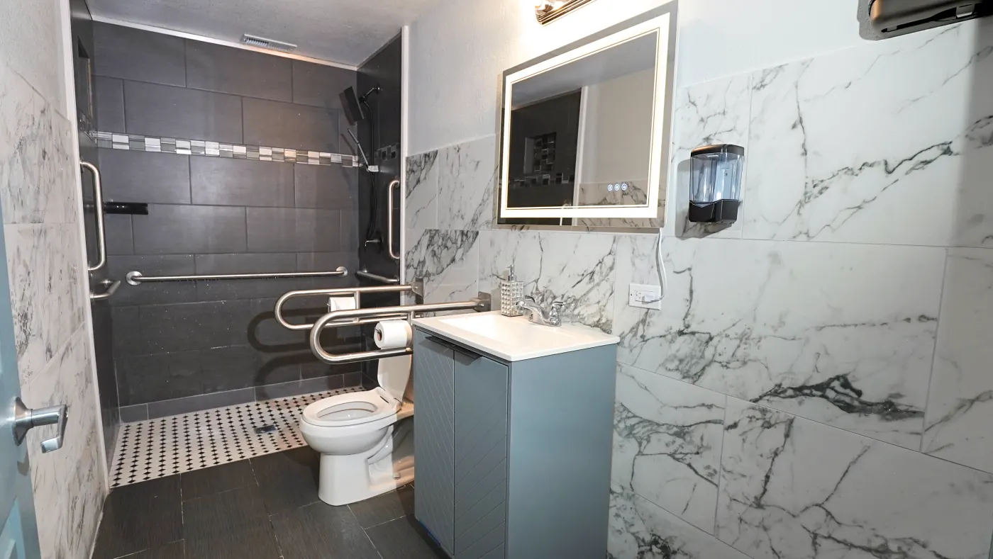 Accessible bathroom with marble walls, grab bars, and walk-in shower